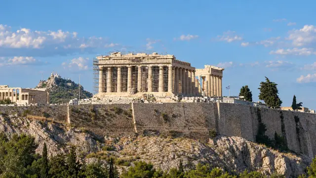 The Parthenon on top of the Acropolis in Athens, with a gap in the middle of its colonnade, seen from a nearby hill
