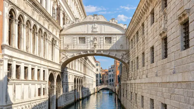 The Bridge of Sighs, an enclosed white stone bridge with two small windows, over a narrow canal in Venice